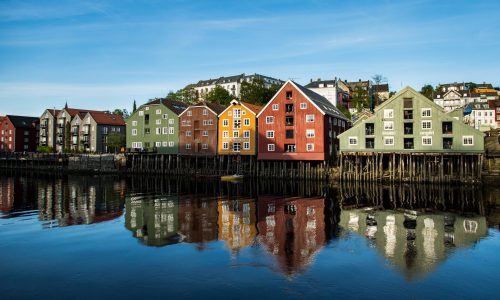 A range of buildings on the shore reflecting in the lake under the clear blue sky